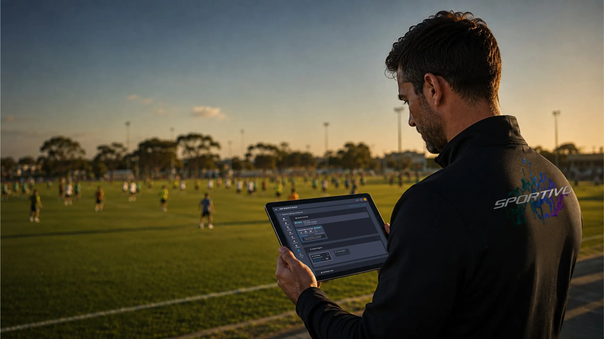 Sports club administrator reviewing live data on a tablet at a multi-field sports complex at dusk